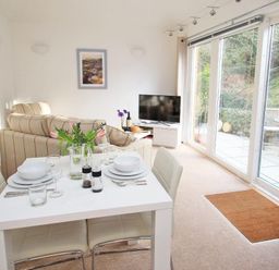 A dining table set for four near a sofa and a television in a living room with glass doors to a patio at Cot Valley Cottage in St Just
