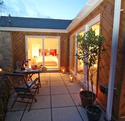 An outdoor patio with a table set for two and potted plants outside a wooden house at Cot Valley Cottage in St Just