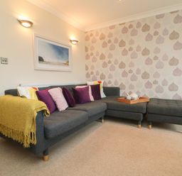 A living room with a grey corner sofa with cushions and a yellow throw and a tray with teapot and cups on the sofa at Ocean Blue in Porthtowan