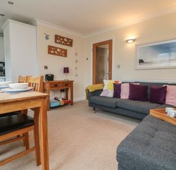 A living room with a dining table and chairs next to a kitchen area with a sofa and cushions at Ocean Blue in Porthtowan
