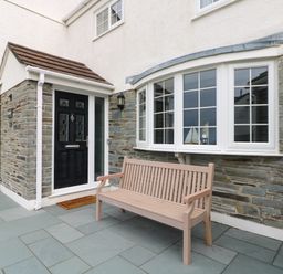 An outdoor area with a black door, a brown bench, and a curved white window at Bayview in Watergate Bay