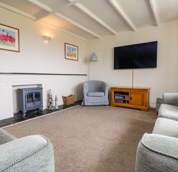 A living room with sofas armchair wood stove and wall mounted tv at Bayview Watergate Bay