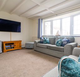 A living room with sofas and cushions a wood TV stand with a TV on the wall and a window with striped curtains at Bayview Watergate Bay