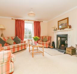 A living room with plaid sofas a wooden coffee table yellow flowers and a fireplace at Goshen Farm in St Agnes