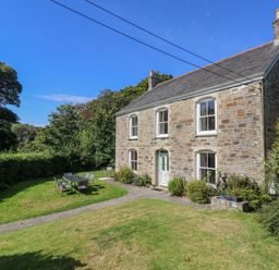 A stone house with a front garden featuring outdoor chairs and table at Goshen Farm in St Agnes