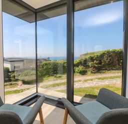 Corner of a room with two chairs facing large windows overlooking a garden path and ocean at Trelawns in Mawgan Porth