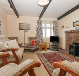 A living room with armchairs a sofa carpet brick fireplace television and floral curtains at Parc An Castle Cottage in Lizard