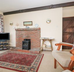 A living room with a brick fireplace television floral curtains and armchairs at Parc An Castle Cottage in Lizard