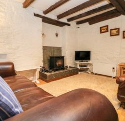 A living room with leather sofas a wood stove a television on a stand and framed pictures on the wall at Apple Loft in Lostwithiel