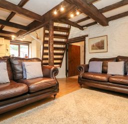 A living room with two leather sofas with striped cushions a rug and wooden stairs at Apple Loft in Lostwithiel