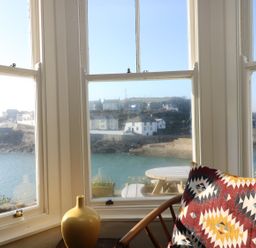 A window view of waterfront houses a round outdoor table and a chair with a patterned cushion at Haven in Porthleven