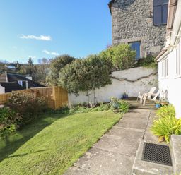 A garden with a lawn a stone path and two chairs by a white building at Cockle Island Cottage in Porthallow