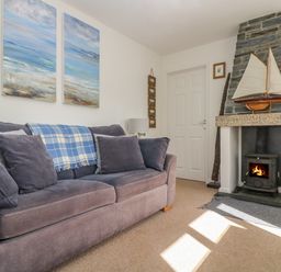 A living room with a sofa a fireplace and paintings on the wall at Cockle Island Cottage in Porthallow