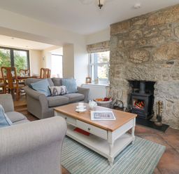 A living room with sofas coffee table and a stone fireplace adjacent to a dining area with wooden chairs and table at Rose Villa in Newlyn