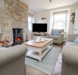 A living room with a stone fireplace a wood stove a coffee table a TV and armchairs at Rose Villa in Newlyn
