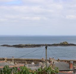 Rooftops and chimneys with a view of a stone pier and rocky island in the sea at Lookout in Mousehole