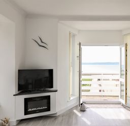 A living room with a wall-mounted tv and fireplace opens to a balcony with a sea view at Sea Breeze in Marazion