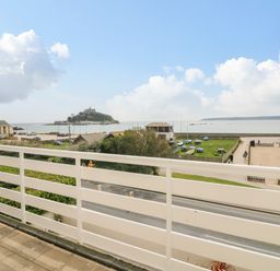 A balcony overlooking a road green area with boats playground and a sea with an island at Sea Breeze in Marazion
