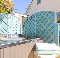 An outdoor hot tub next to blue lattice privacy screens with folded towels on a small table at Respryn Mevagissey