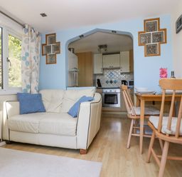 A living room with a white sofa with blue cushions a wooden dining table with chairs and a kitchen visible through an archway at Respryn Mevagissey