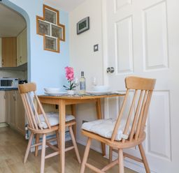 A small dining area with a wooden table and two chairs next to a kitchen and a white door at Respryn in Mevagissey