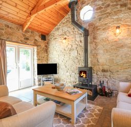 A living room with stone walls a wood burning stove a coffee table and two sofas at Pond Cottage in Stithians