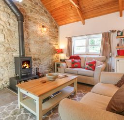 A living room with a fireplace stone wall wooden ceiling two sofas a wooden coffee table and shelves at Pond Cottage in Stithians