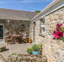 A stone patio with wooden chairs and table with cups and a blanket and potted plants at Pond Cottage in Stithians