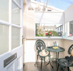 A small enclosed patio with metal chairs and table with decorative boats and flowers at Calac Cottage in Mousehole