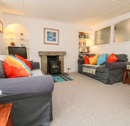A living room with two sofas with colorful cushions a fireplace and bookshelves at Calac Cottage in Mousehole