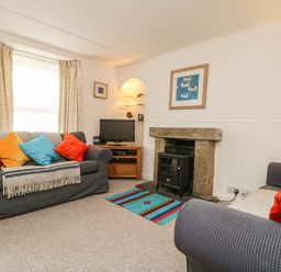 A living room with sofas cushions a fireplace a television and a bookshelf at Calac Cottage in Mousehole