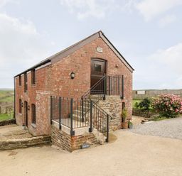A brick building with stairs and a black metal railing outside surrounded by greenery at Castle Dore Barn in Fowey