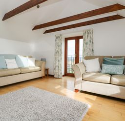 A living room with two beige sofas pillows and wooden beams at Castle Dore Barn in Fowey