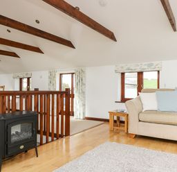 A living room with a beige sofa wooden side table windows and exposed wooden ceiling beams at Castle Dore Barn in Fowey