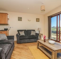 A living room with two sofas a wooden coffee table with a vase and bowl a side table with a lamp and sliding glass doors leading outside at Surfside in Marazion