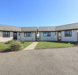 Two single-story houses with tiled roofs and grass lawns connected by a paved path at Surfside in Marazion