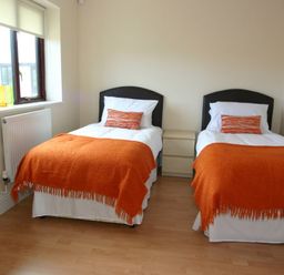 A bedroom with two single beds orange throws and pillows between a window and a nightstand at Sea Shore in Marazion