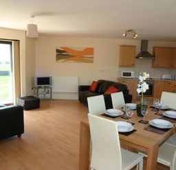 An open plan living and kitchen area with dining table set for six and two black sofas at Sea Shore in Marazion