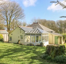 A house with a glass conservatory surrounded by trees and grass at Boskednan Wartha in Penzance