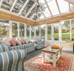 A sunroom with striped sofas, a coffee table with fruit on a rug, and a television at Boskednan Wartha in Penzance