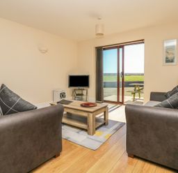 A living room with two sofas a wooden coffee table a television and sliding glass door leading outside at Seashells in Marazion