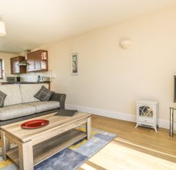 A living room with a sofa coffee table and television with a kitchen in the background at Seashells in Marazion