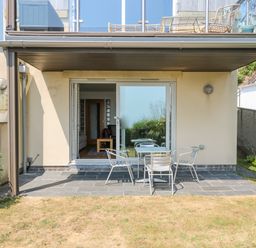 A patio area with a table and four chairs outside sliding glass doors at Rock Pool in Downderry