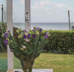 A bouquet of flowers on a table in front of a window showing a garden hedge and the sea beyond at Rock Pool in Downderry