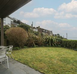 A garden with grass lawn metal table and chairs and houses in the background at Rock Pool in Downderry