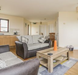A living room with two sofas a wooden coffee table with an orange vase and a dining area at Shoreline in Marazion