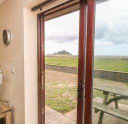 A view of an open glass door showing a picnic table outside and a clock lamp and table inside at Shoreline in Marazion