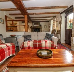 A living room with wooden beams on the ceiling sofas with plaid blankets and a wooden coffee table with a metallic bowl at Chenalls Cottage in Helston
