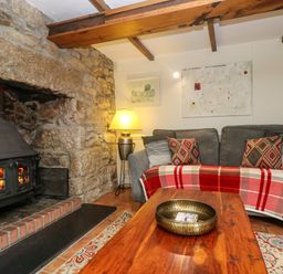 A living room with a wood stove fireplace a sofa with patterned cushions a red plaid throw and a wooden coffee table at Chenalls Cottage in Helston
