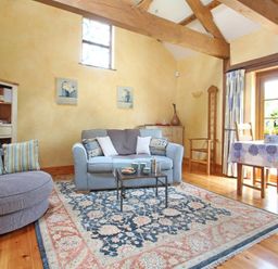 A living room with sofas a coffee table a rug wooden beams and a dining table at Summer House in Helston